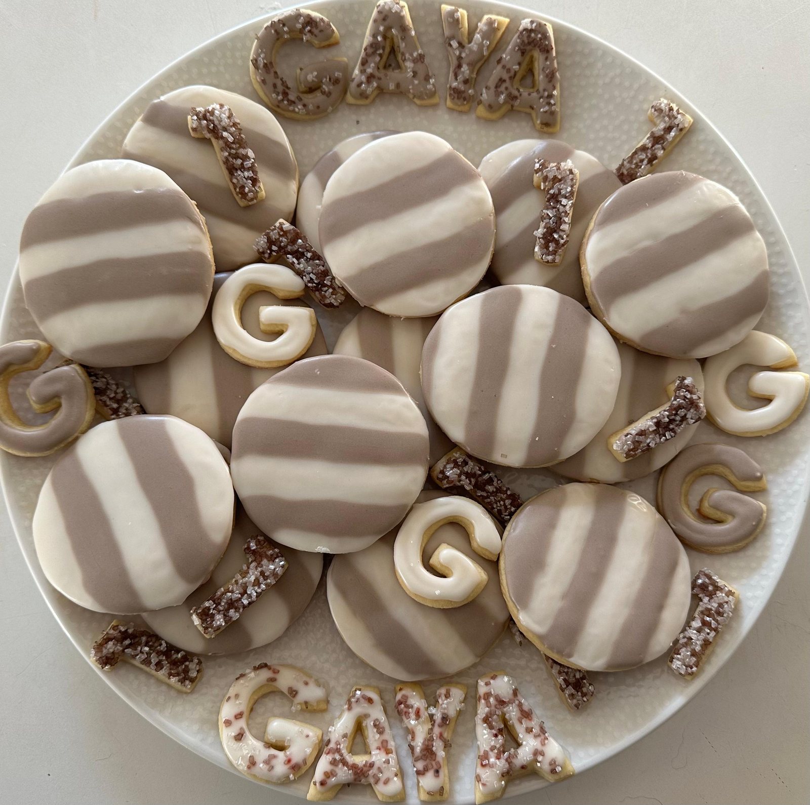 Neutral first birthday cookies with striped circles, number ones, and letter cookies